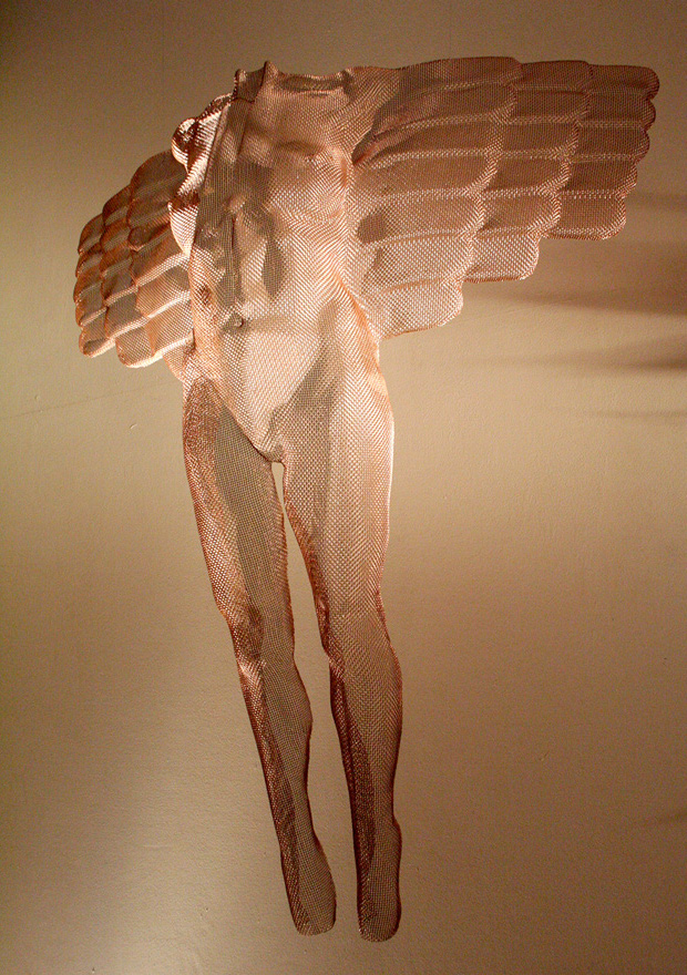 A bronze angel figure as a modern wall sculpture reflecting projected light on a golden background