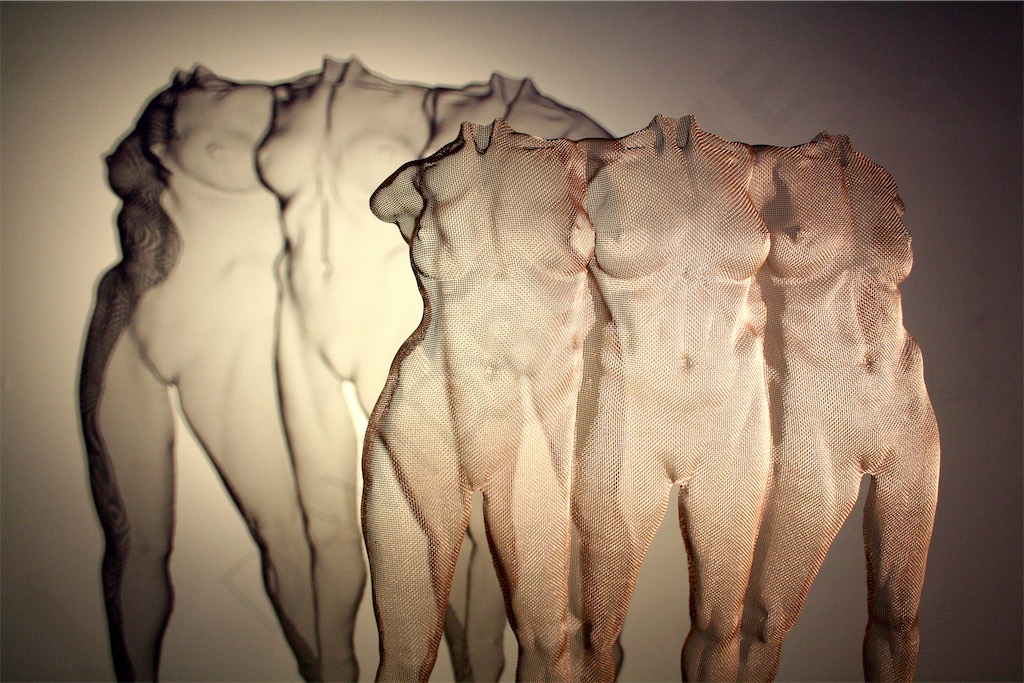 A rose-gold wire sculpture depicting three figures with shadow projections - artwork by David Begbie